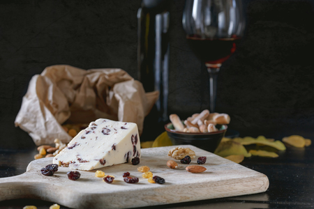 Wensleydale cheese with cranberries, red wine, honey, nuts, raisins on wooden cutting board. Black concrete background. Selective focus.の写真素材