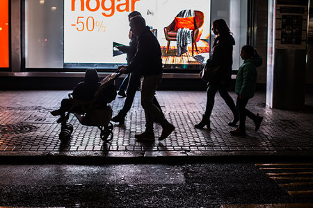 Seville, Spain - January 13, 2018: Silhouette of family shopping in the center of the city. Family in the sales. Neon signs and billboard advertisements behind. Twice a year in Spain shoppers are treated to an end-of-season sale period, called las rebajasのeditorial素材