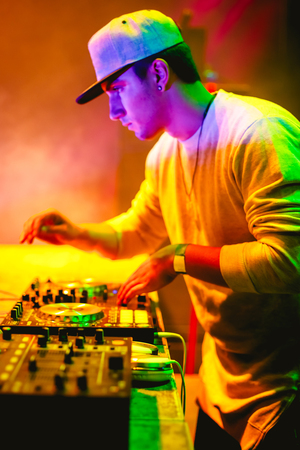 Portrait of Young DJ playing mixing music at night party under colorful lights. Fun, youth, entertainment and fest concept. の写真素材