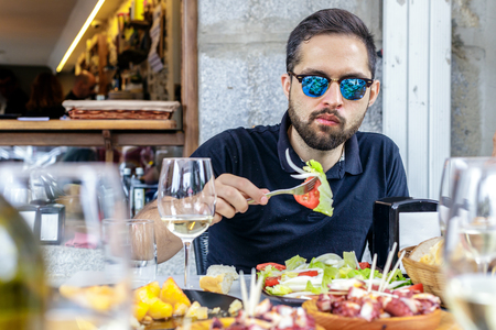 Young man eating vegetable salad and pulpo a la Gallega with potatoes. Galician octopus dishes. Famous dishes from Galicia, Spain.の写真素材