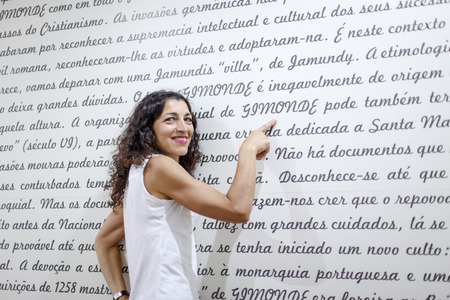 Portrair of beautiful young woman pointing a finger at the word Gimonde on a wall with the written...