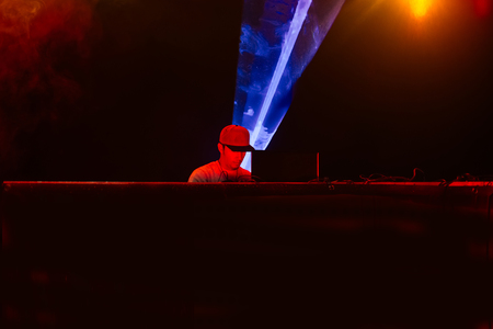 Dj playing mixing music at night party under blue and red lights. Fun, youth, entertainment and fest concept. の写真素材