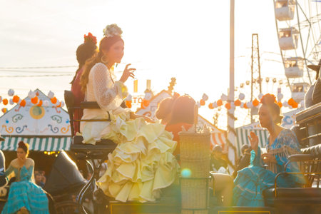 Seville, Spain - May 03, 2017:  Women dressed in traditional costumes riding horse carriages at sunset and celebrating at Seville's April Fairのeditorial素材
