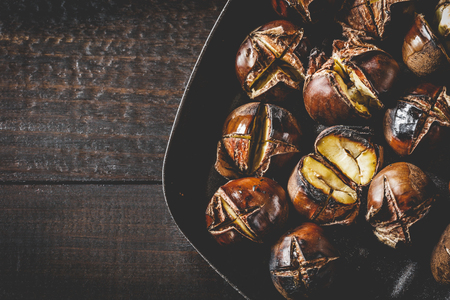 Roasted edible chestnuts in cast iron skillet over rustic wooden table.の写真素材