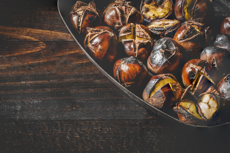 Close-up of Roasted chestnuts in iron grilling pan over rustic wooden table with copy space.の写真素材