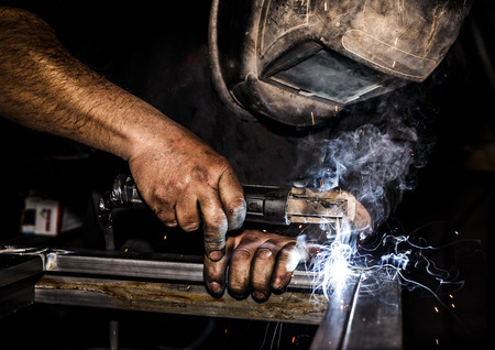 Profesional welder in protective mask welding metal and sparks metal.