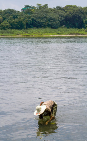Guilin, China - July 13, 2010: Chinese man looking for clams in the Li river. Guilin has a rich variety of local dishes and an abundance of good restaurants. The Li River, or Li Jiang, is in Guilin, in South Chinaâs Guangxi Province. It is renowned as bのeditorial素材