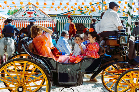 Sevilla, Spain - April 18, 2018: Spanish families in traditional dress travelling in a horse drawn carriages at the April Fair, Seville Fair (Feria de Sevilla). The Seville Fair (officially and in Spanish: Feria de abril de Sevilla, "Seville April Fair") のeditorial素材