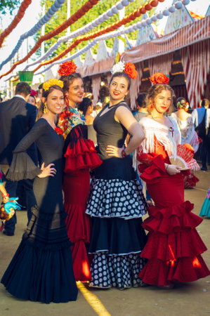 Sevilla, Spain - April 18, 2018: Beautiful women in traditional and colorful dress enjoy April Fair, Seville Fair (Feria de Sevilla). The Seville Fair (officially and in Spanish: Feria de abril de Sevilla, "Seville April Fair") is held in Andalusian capitのeditorial素材