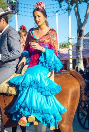 Sevilla, Spain - April 18, 2018: Beautiful andalusian young woman with traditional dress riding horses at the Seville's April Fair, Seville Fair (Feria de Sevilla). The Seville Fair (officially and in Spanish: Feria de abril de Sevilla, "Seville April Faiのeditorial素材