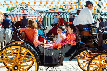 Sevilla, Spain - April 18, 2018: Spanish families in traditional dress travelling in a horse drawn carriages at the April Fair, Seville Fair (Feria de Sevilla). The Seville Fair (officially and in Spanish: Feria de abril de Sevilla, "Seville April Fair") のeditorial素材