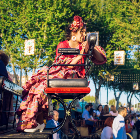 Sevilla, Spain - April 18, 2018: Beautiful woman in traditional and colorful dress travelling in a horse drawn carriages at the April Fair, Seville Fair (Feria de Sevilla). The Seville Fair (officially and in Spanish: Feria de abril de Sevilla, "Seville Aのeditorial素材