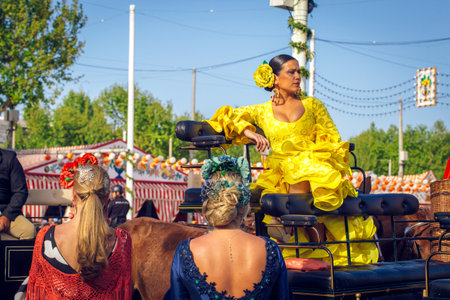 Seville, Spain - April 19, 2018: Attractive woman in traditional dress travelling in a horse drawn carriages at the April Fair, Seville Fair (Feria de Sevilla). The Seville Fair (officially and in Spanish: Feria de abril de Sevilla, "Seville April Fair") のeditorial素材