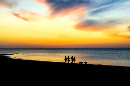 Silhouettes of people walking on the beach at sunset.の写真素材