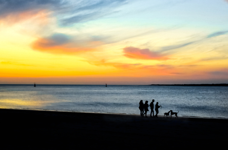 Silhouettes of people walking on the beach at sunset.の写真素材