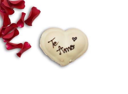 Festive dessert in the shape of a heart with text I love you in Spanish and rose petals isolated on white.の写真素材