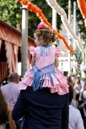 Seville, Spain - May 09, 2019 : Little girl sitting on his father shoulders at the April Fair (Feria de Abril), Seville Fair (Feria de Sevilla), Andalusia, Spainのeditorial素材