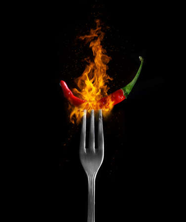 Red hot chili pepper with flame on fork and black background.の写真素材