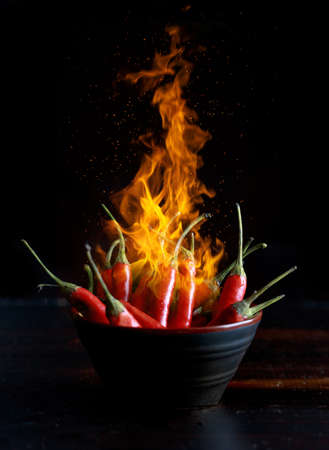 Red hot chili peppers bowl with flame and black background.