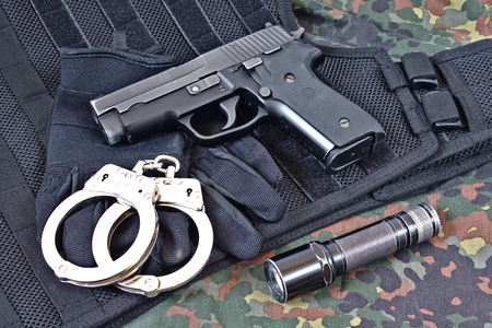 Handgun with handcuffs, gloves and flashlight on black tactical vest and camouflage clothingのeditorial素材