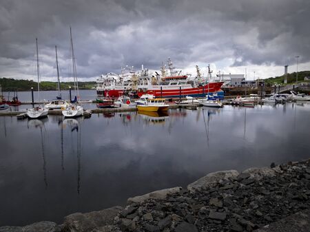Killybegs, Co. Donegal, Ireland - May 19th, 2019 - Harbour with yachts, fishing vessels, overcast sky and stone quay in the foreground.のeditorial素材