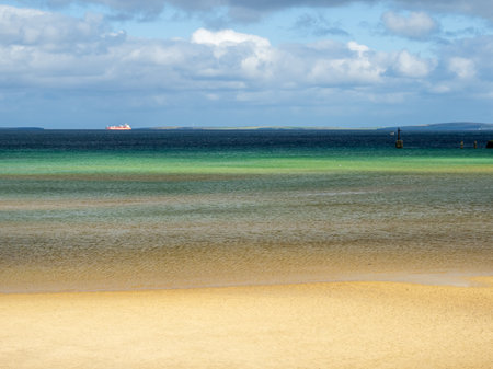 View of sandy beach with turqoise shallow water and dark blue deep water of Scapa Flow in the backgroundの写真素材
