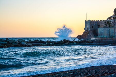 in a quiet night a wave crash on the rocks, at sunset hour in Genoaの写真素材