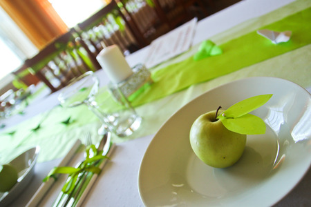 A detail picture of the table prepared for wedding lunch. All  accessory is in green color. The fresh green apple is on the plate.の写真素材
