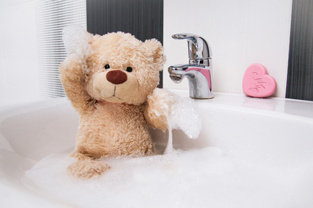 A cute teddy bear is sitting in the basin and washing.の写真素材