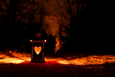 A detail of the lantern with heart shaped window on the snow on a narrow forest road. The forest skyline is behind.の写真素材