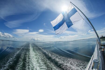 A picture of a wake behind the big ferry ship from Finland. The flag is hanging behind and waving in the air.の写真素材