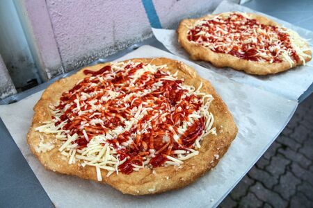 The typical street food from middle Europe (Hungary, Czech Republic or Slovakia) called "LangoÅ¡". Donut pastry fried and covered with cheese, ketchup and garlic.の写真素材