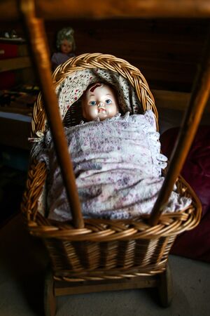 The unused old doll with a hole in its head is lying in the baby carriage and looking quite scary and depressive.の写真素材