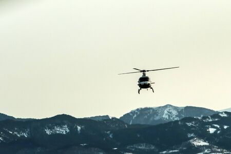 An atmospheric picture shows the helicopter climbing in front of the high snowy mountains.