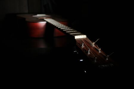A shaded picture of a guitar. It lies in the dark with only a part visible under small amount of...