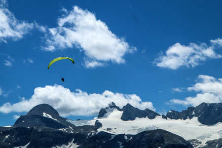 The paraglides are flying above the mountains high in the blue sky and enjoying the view.の写真素材