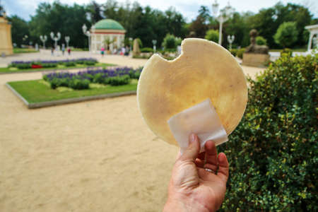 The hand is holding the traditional Czech round spa wafer at the spa city promenade.