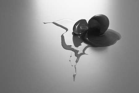 The fallen organic egg lies broken with the eggshell smashed and yolk and white flowing out of it. A...