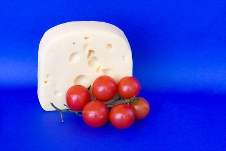 Food & Drinks - Cheese. Piece of soft creamy bavarian cheese with cherry tomatoes isolated on blue background.の写真素材