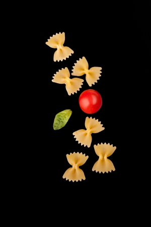 Pasta Varieties - Farfalle pasta, cherry tomato and basil leaf, isolated on black  background の写真素材