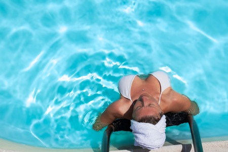 Middle aged Caucasian woman relaxing in blue transparent water at spa.の写真素材