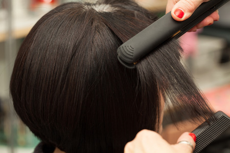 Hair straightening by a hairdresser in a professional salon, closeup shot.の写真素材