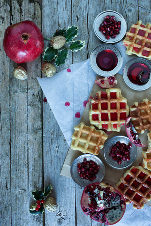 Christmas table with fresh baked waffle and pomegranate sorbet decorated with holly and pomegranate seeds.の写真素材