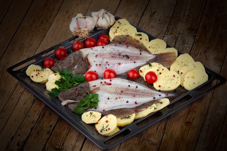 Tray with raw turbot fish and potatoes on wood background, ready to bake.