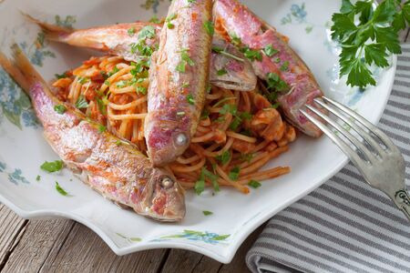 Closeup of plate with spaghetti and red mullet fish, traditional recipe of the Italian cuisine.