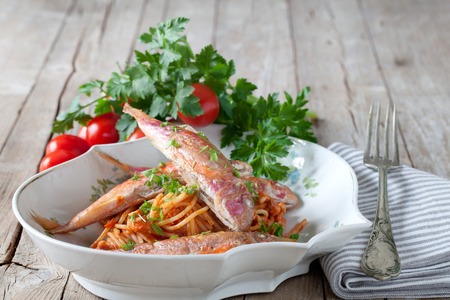 Plate with spaghetti dressed with red mullet sauce, decorated with parsley and cherry tomatoes.