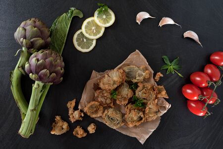 Fried artichokes on kitchen paper, decorated with slices of lemon, mint leaves, garlic and Pachino tomatoes.の写真素材