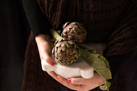 Woman hands holding marble mortar with  fresh artichokes from the garden.の写真素材