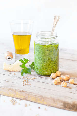 Jar with parsley pesto and ingredients to prepare it: parsley, parmesan cheese, extra virgin olive oil, hazelnuts and white pepper.の写真素材