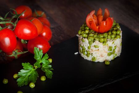 Portion of risotto with peas on slate plate, decorated with tomatoes and parsley.の写真素材